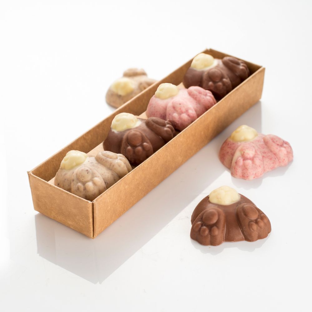 Row of four digging chocolate bunnies, with tails and feet in the air. Two with milk chocolate, one cookies and cream, and one raspberry white chocolate. All feature white chocolate tails.
